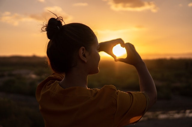 girl making a heart with her hands toward the sun